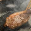 A juicy steak sizzling on a cast iron skillet, being flipped with chopsticks.