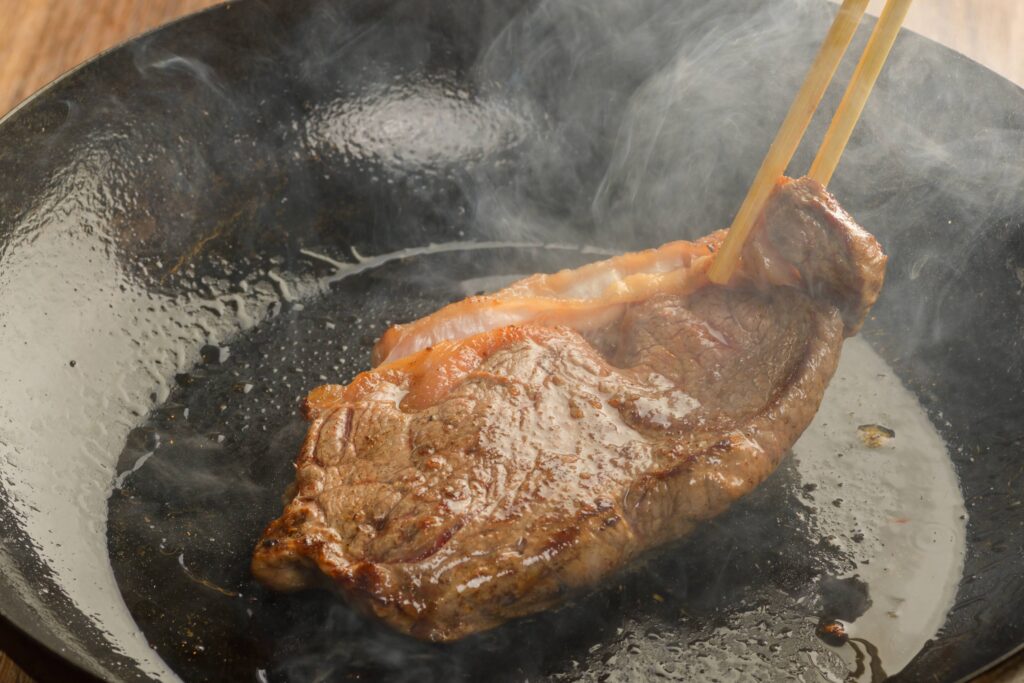 A juicy steak sizzling on a cast iron skillet, being flipped with chopsticks.